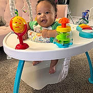 Nessiah is registered to the contest to win money with this photo: baby, child, infant, smiling, happy, portrait, sitting, activity_center, baby_toys, colorful_toys, playtime, indoor, home, carpet, high_chair, green_shirt, curly_hair, toys, family, cute