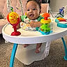 baby, child, infant, smiling, happy, portrait, sitting, activity_center, baby_toys, colorful_toys, playtime, indoor, home, carpet, high_chair, green_shirt, curly_hair, toys, family, cute