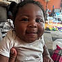 Kemet Brooks is registered to the contest to win money with this photo: baby, smiling, child, curly_hair, onesie, hand, living_room, toys, orange_wall, lamp, picture_frames, plaid_pillow, carpet, furniture, person, indoor, closeup, happy, infant, cozy