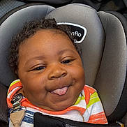 Kemet Brooks is registered to the contest to win money with this photo: baby, child, car_seat, tongue_out, smile, curly_hair, colorful_clothing, striped_shirt, black_blanket, cute, playful, infant, seatbelt, comfort, closeup, face, happy, indoors, person, portrait