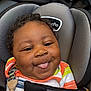 baby, child, car_seat, tongue_out, smile, curly_hair, colorful_clothing, striped_shirt, black_blanket, cute, playful, infant, seatbelt, comfort, closeup, face, happy, indoors, person, portrait