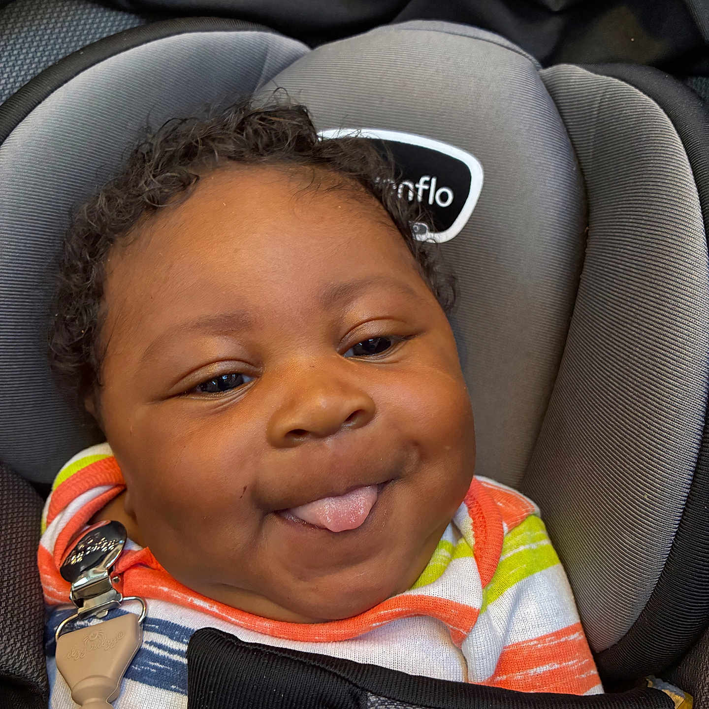 Kemet Brooks is registered to the contest to win money with this photo: baby, black_blanket, car_seat, child, closeup, colorful_clothing, comfort, curly_hair, cute, face, happy, indoors, infant, person, playful, portrait, seatbelt, smile, striped_shirt, tongue_out
