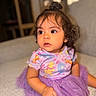 Catalina is registered to the contest to win money with this photo: baby, child, toddler, portrait, sitting, bed, indoors, purple_dress, tutu, colorful_clothing, cartoon_pattern, curly_hair, hair_bun, brown_eyes, curious, sunlight, warm_lighting, soft_focus, home, photography