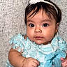 baby, child, portrait, sitting, turquoise_dress, white_bow, headband, frilly_clothing, wide_eyes, serious_expression, infant, face, hands, indoor, fabric_backdrop, close_up, adorable, photography, formal_outfit, baby_dress