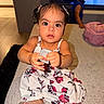 Catalina is registered to the contest to win money with this photo: child, baby, toddler, girl, boy, portrait, sitting, floral_dress, hair_bows, smiling, indoors, living_room, couch, television, toy, device, pink_suitcase, home, shoes, family