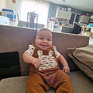 James participe au concours pour gagner de l'argent avec cette photo : baby, smile, couch, living_room, overalls, child, indoor, furniture, happy, foot, clothing, person, home, table, chair, plant, window, kitchen, light, interior