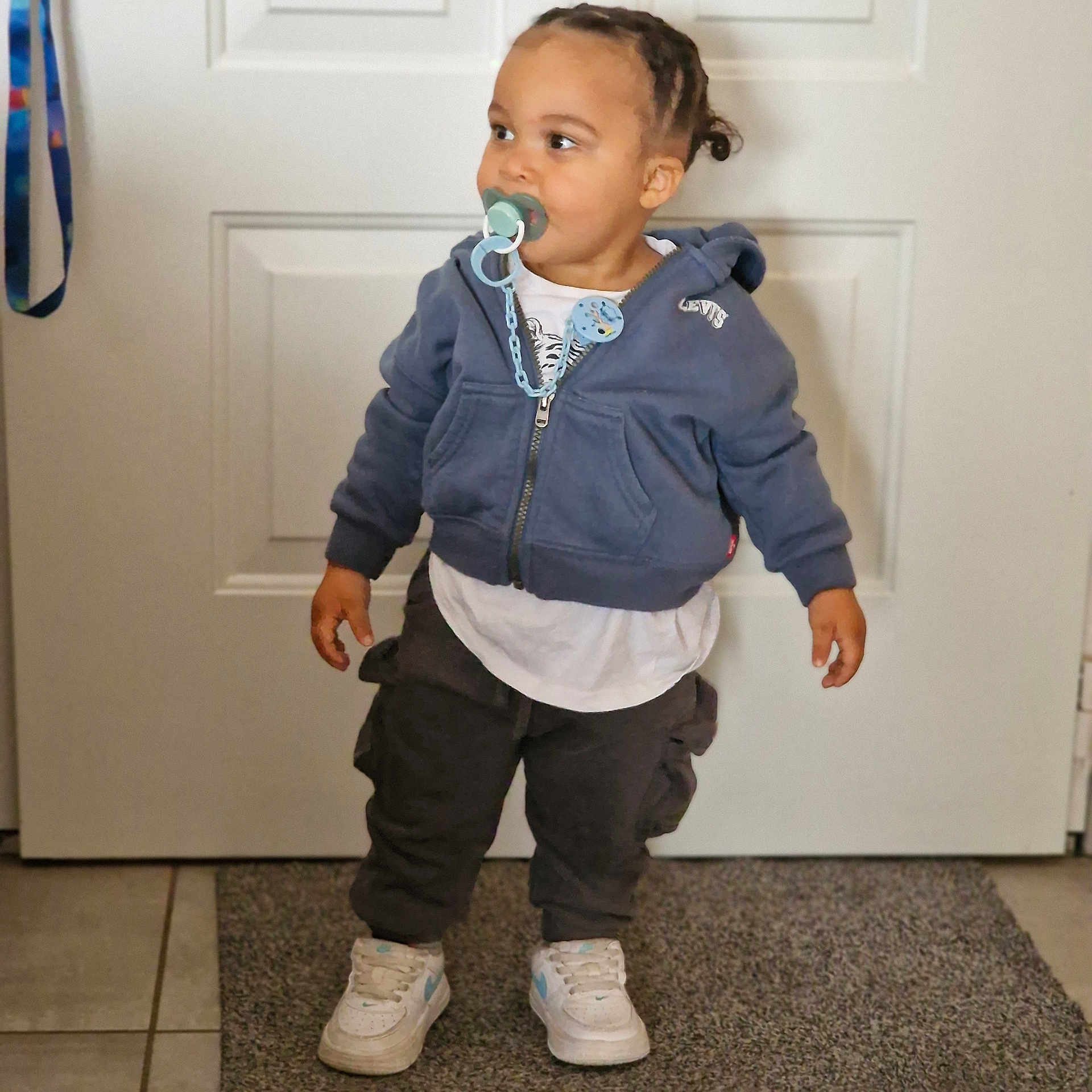 James a rejoint le concours — aidez-le/la à gagner de superbes lots ! toddler, child, pacifier, hoodie, braided_hair, sneakers, indoors, door, carpet, pants, white_shirt, standing, levis, cute, young_child, floor_tiles, clothing, person, home, curious