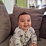 baby, child, infant, smiling, tongue_out, onesie, mickey_mouse, rattle, toy, couch, pillow, indoor, cute, happy, sitting, playful, face, hand, foot, home