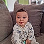 James participe au concours pour gagner de l'argent avec cette photo : baby, onesie, mickey_mouse, toy, couch, pillow, child, infant, cute, tongue_out, sitting, indoors, clothing, hand, face, smile, furniture, playful, comfortable, young