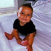 Luka joined the competition — help win amazing prizes! baby, child, infant, smile, black_clothing, bed, white_bedspread, indoor, window, blinds, cabinet, foot, hand, curious_look, cheeky_smile, sitting, portrait, room, cozy, young_kid