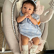 Emma Peña Bello is registered to the contest to win money with this photo: baby, infant, child, cute, dress, blue_dress, socks, bows, headband, baby_seat, blanket, indoor, carpet, person, soft_toys, cushion, hands, face, lying_down, cozy