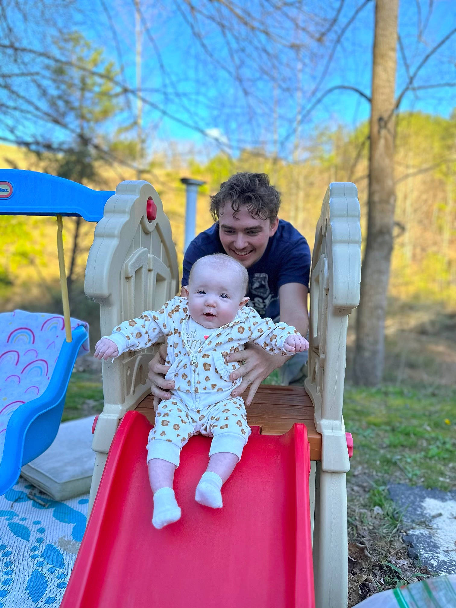 Oaklee is registered to the contest to win money with this photo: baby, baby_toddler_clothing, blue, chute, city, event, fun, grass, happy, joy, leisure, outdoor_play_equipment, person, plant, playground, playground_slide, public_space, recreation, sitting, sky