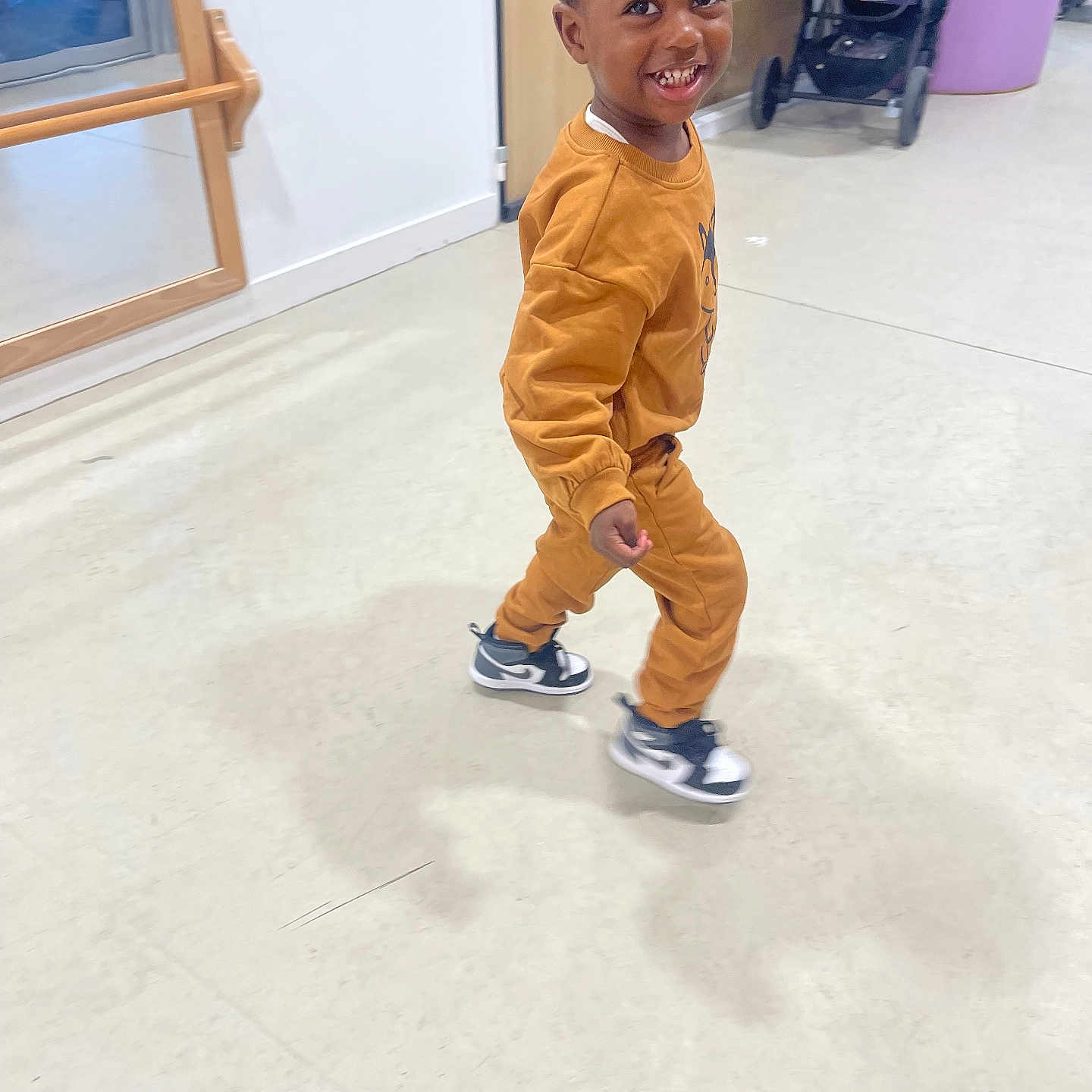 Lansana participe au concours pour gagner de l'argent avec cette photo : casual_wear, child, cute, door, floor, happy, indoor, mirror, motion, orange_clothing, person, play_area, shoe, smiling, sneakers, stroller, toddler, walking, wall, young_child