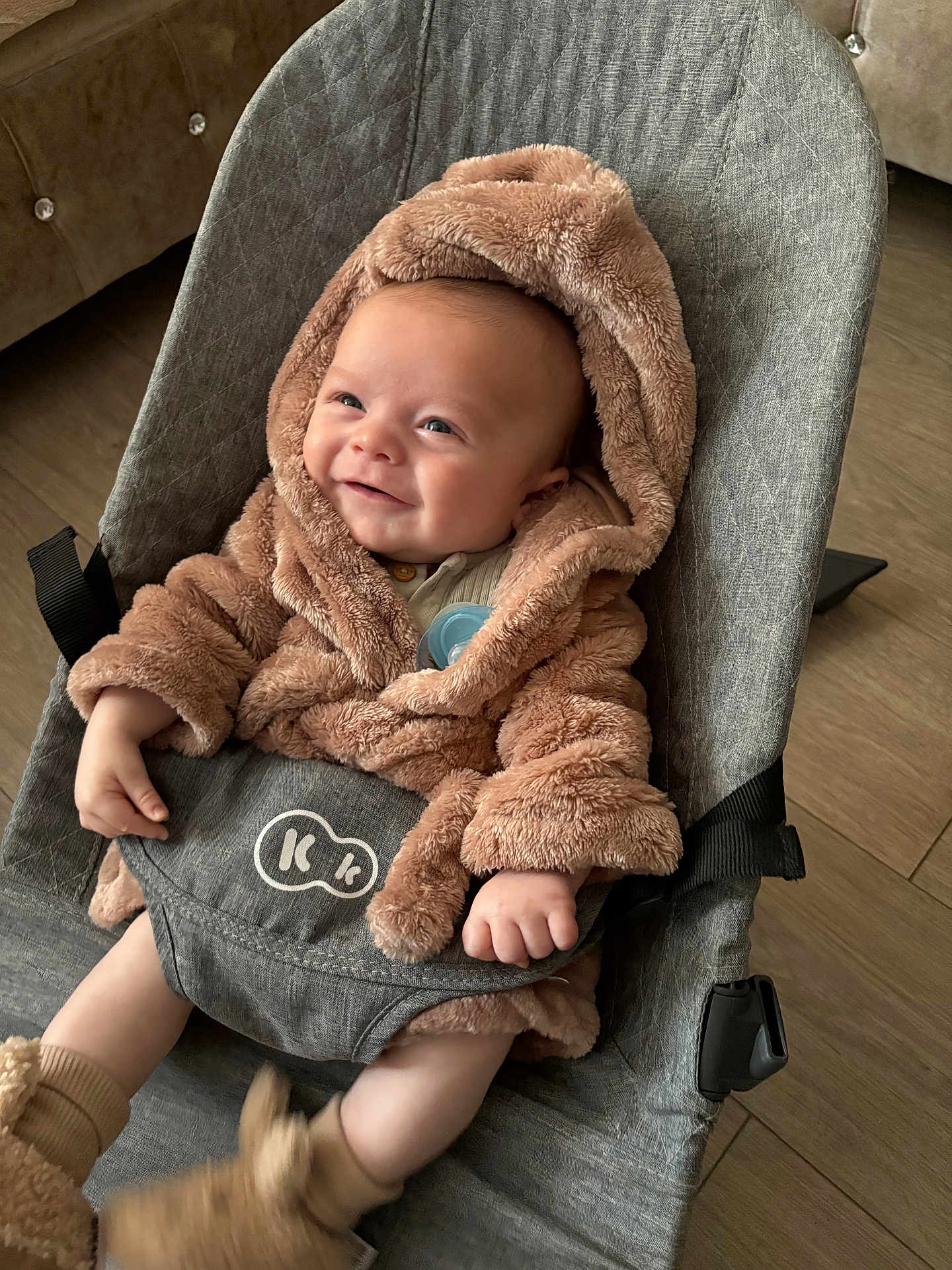 Arlo is registered to the contest to win money with this photo: baby, smiling, fluffy_robe, booties, baby_rocker, gray_fabric, indoor, wooden_floor, pacifier, cute, infant, child, happy, seated, cozy, warm_clothing, hands, face, head, soft_texture
