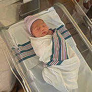 Isaiah is registered to the contest to win money with this photo: newborn, baby, hospital, bassinet, blanket, hat, sleeping, infant, person, bed, healthcare, swaddled, resting, indoor, medical, soft_light, quiet, care, patient, newborn_baby