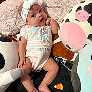 Raelynn joined the competition — help win amazing prizes! baby, infant, headband, bow, onesie, plush_toy, cow_plush, pink_blanket, soft_toy, cute, child, indoors, lying_down, expression, surprised, small_person, cozy, comfort, toddler, home