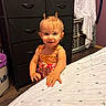 toddler, child, baby, smiling, portrait, indoors, bedroom, dress, hair_buns, standing, face, person, bed, dresser, drawers, laundry, baby_gate, home, furniture, photography