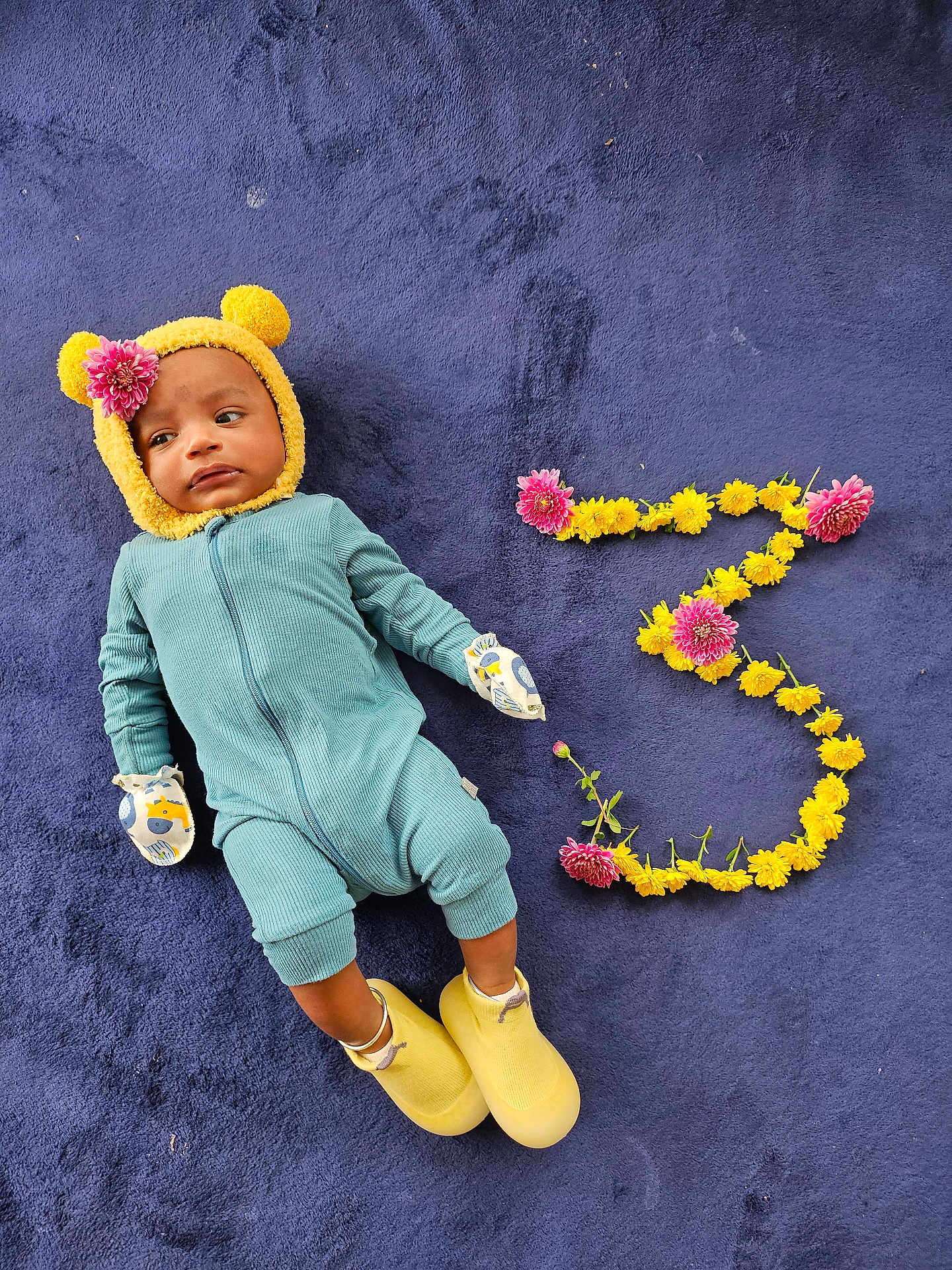 Aditya is registered to the contest to win money with this photo: baby, child, blue_onesie, yellow_hat, flower, purple_blanket, mittens, yellow_shoes, number_three, flower_arrangement, lying_down, cute, milestone, portrait, infant, soft_texture, colorful, celebration, young_child, indoors