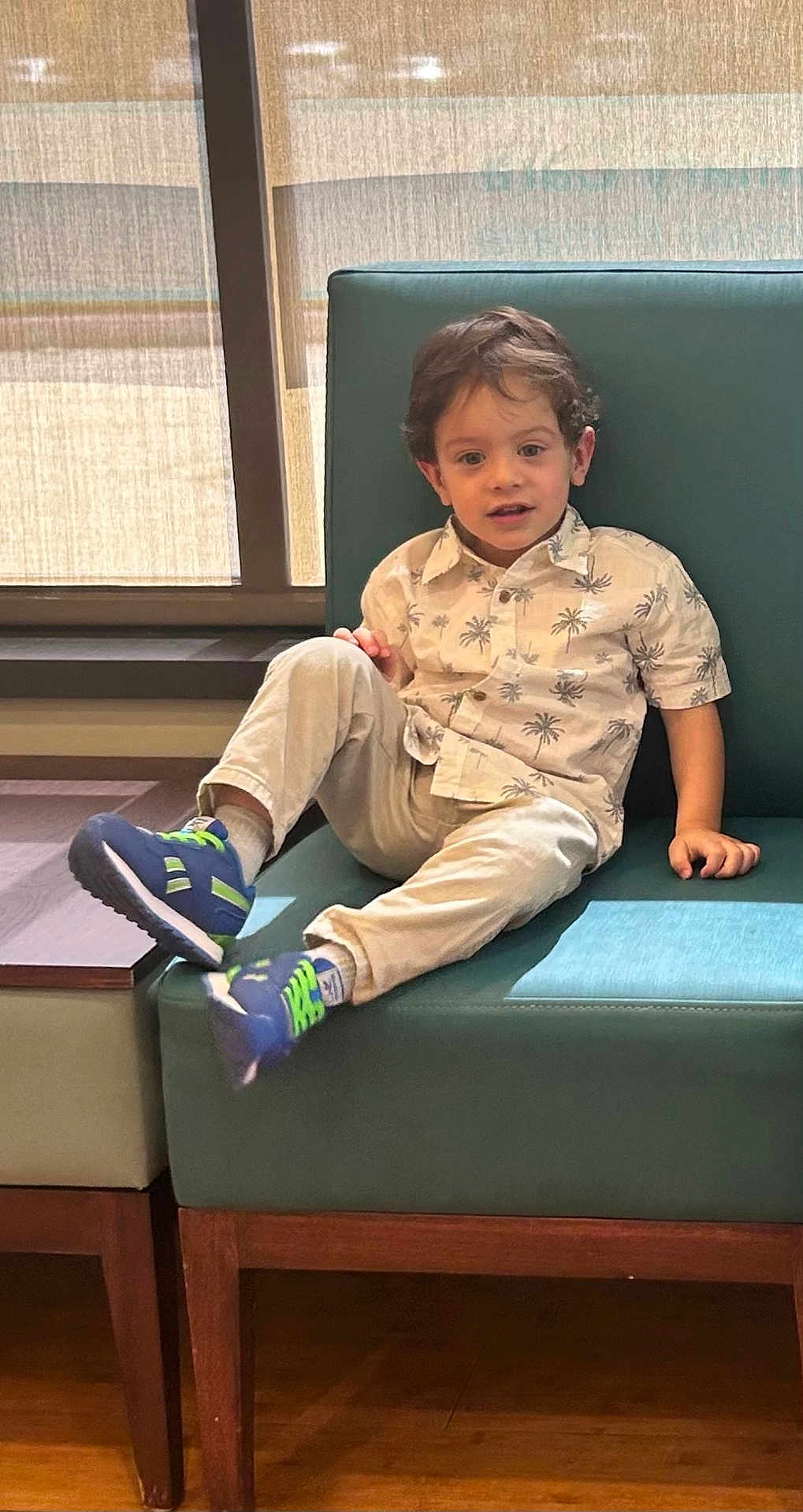 Matthew joined the competition — help win amazing prizes! child, boy, indoor, bench, window, curtains, casual_clothing, palm_tree_pattern, sneakers, blue_shoes, beige_pants, teal_cushion, wood_floor, light, smiling, hair, face, relaxed, seated, daylight
