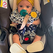 Amilyah is registered to the contest to win money with this photo: baby, infant, child, car_seat, yellow_bow, floral_outfit, pacifier, headband, sitting, portrait, face, eyes, car_interior, vehicle, harness, safety_seat, shoes, cute, indoor, photography