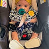 baby, infant, child, car_seat, yellow_bow, floral_outfit, pacifier, headband, sitting, portrait, face, eyes, car_interior, vehicle, harness, safety_seat, shoes, cute, indoor, photography