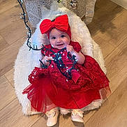 Cora joined the competition — help win amazing prizes! baby, child, red_dress, headband, bow, christmas_lights, holiday, smiling, indoor, flooring, wooden_floor, decorations, christmas_tree, festive, cushion, white_fur, cute, happy, portrait, toddler