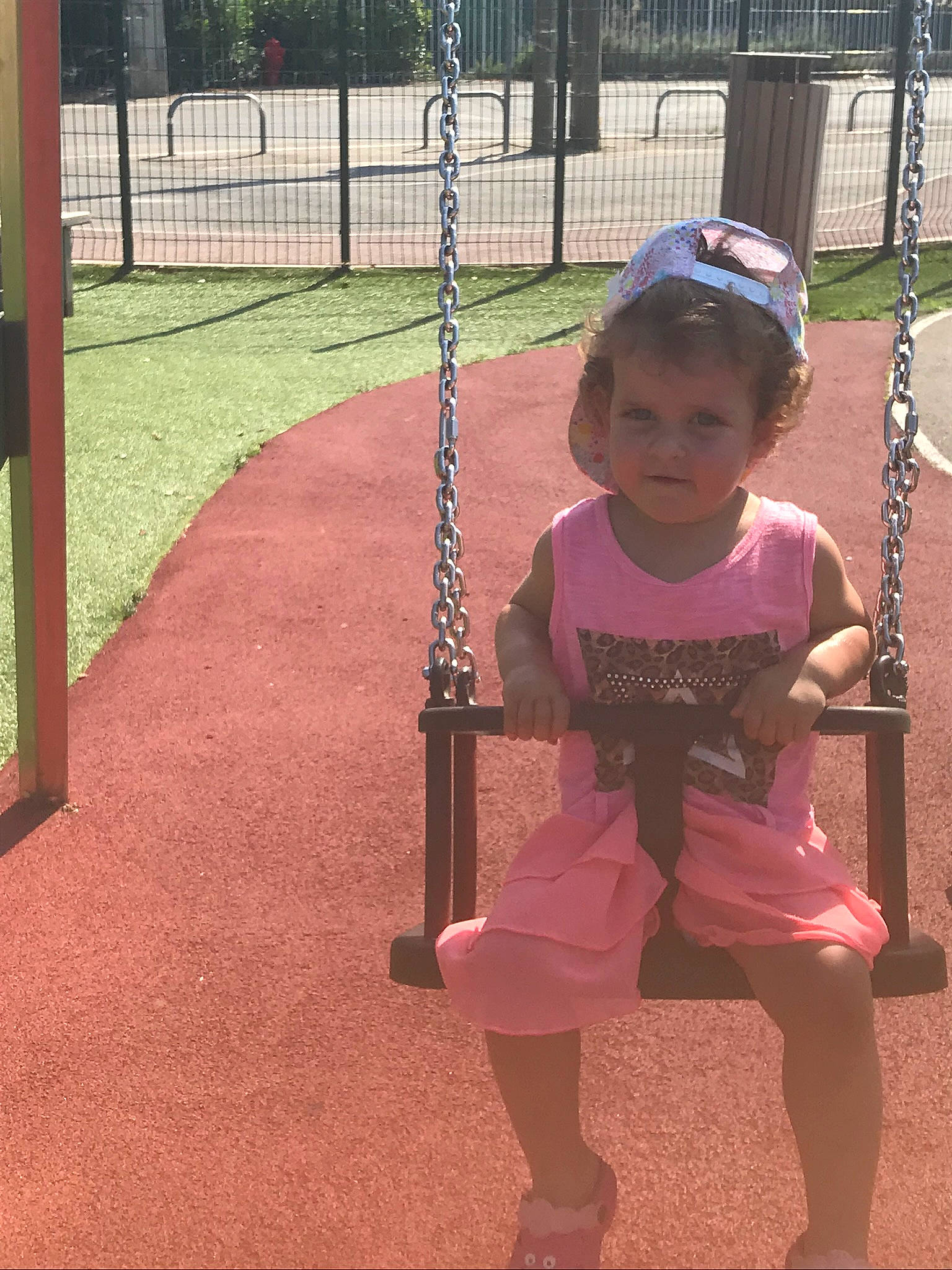 Loona a rejoint le concours — aidez-le/la à gagner de superbes lots ! baby_toddler_clothing, child, city, fence, flooring, fun, grass, happy, hat, leisure, outdoor_play_equipment, person, pink, play, playground, recreation, sandal, sleeve, swing, t_shirt