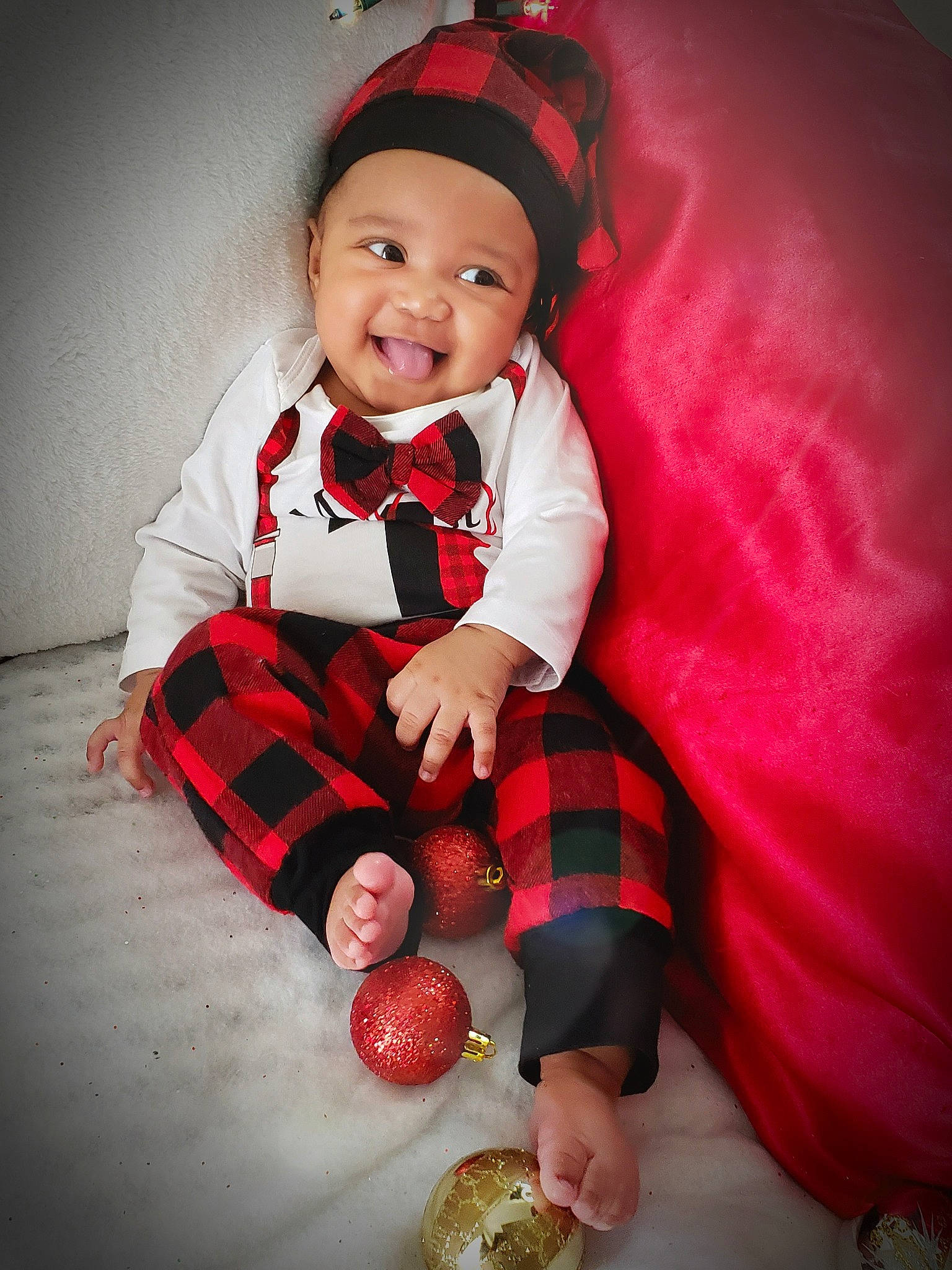 Amari is registered to the contest to win money with this photo: baby, baby_laughing, baby_toddler_clothing, carmine, child, christmas, costume_accessory, cricket_ball, eye, headwear, joy, laugh, mouth, nose, overall, pattern, person, plaid, pleased, produce
