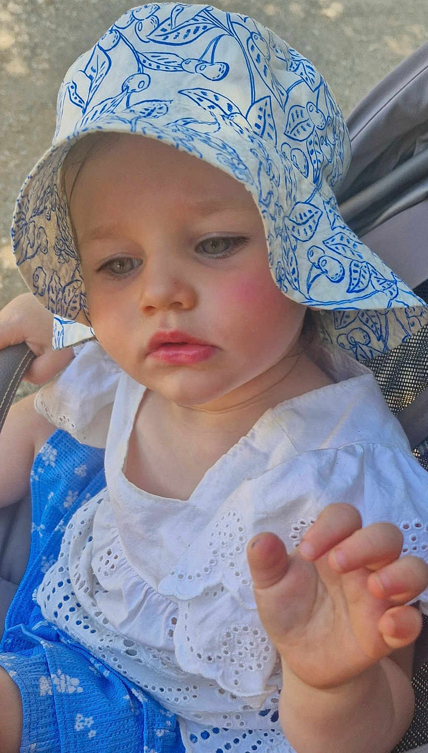 Lara participe au concours pour gagner de l'argent avec cette photo : toddler, child, baby, hat, sunhat, white_clothing, blue_clothing, stroller, hand, face, outdoor, young_child, cute, eyelet_fabric, summer, closeup, expression, skin, portrait, sitting