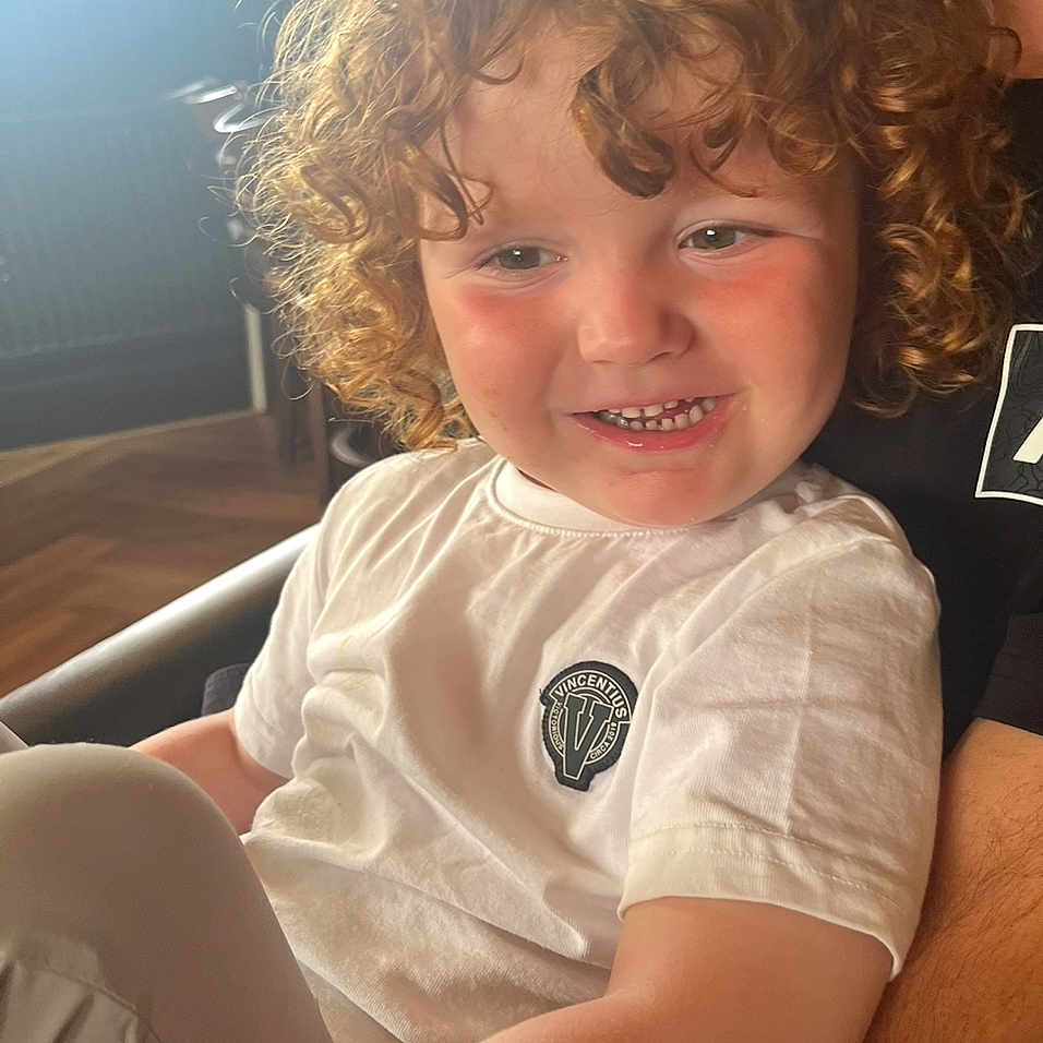 Ojay is registered to the contest to win money with this photo: casual_clothing, child, closeup, cozy, curly_hair, cute, face, happy, indoor, logo, natural_light, person, portrait, rosy_cheeks, sitting, smiling, toddler, warm_light, white_shirt, young