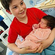 Myriam a rejoint le concours — aidez-le/la à gagner de superbes lots ! child, baby, newborn, boy, infant, smiling, holding, indoor, red_shirt, pink_clothing, bed, blanket, hospital_room, family, portrait, happy, person, cute, resting, toddler