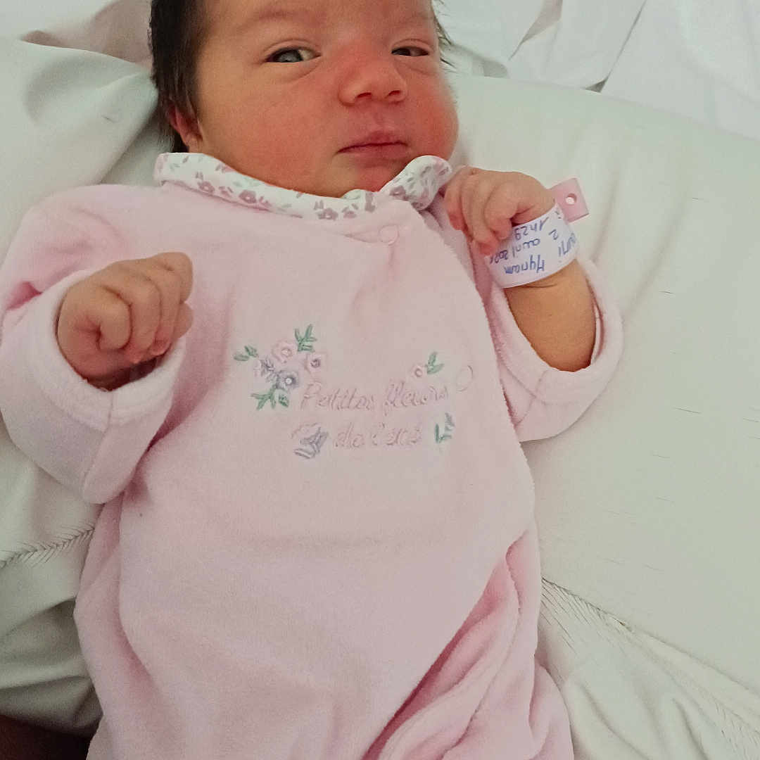 Myriam a rejoint le concours — aidez-le/la à gagner de superbes lots ! newborn, baby, infant, pink_onesie, sleeping, bed, white_sheets, hospital_bracelet, person, indoor, cute, small, face, hand, portrait, cozy, child, soft, resting, healthcare