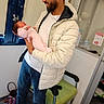 Myriam a rejoint le concours — aidez-le/la à gagner de superbes lots ! man, baby, newborn, holding, white_jacket, pink_clothing, indoor, chair, bag, floor, smiling, window, jeans, sneakers, person, portrait, parent, child, tenderness, family