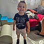 child, toddler, smiling, indoor, casual_clothing, shorts, sneakers, curtains, couch, blanket, floor, window, toy, footwear, person, happy, hairstyle, living_room, home, sunlight
