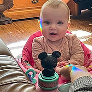 Luci is registered to the contest to win money with this photo: baby, child, pink_baby_seat, toy, mickey_mouse, rainbow_reflection, hand, wooden_floor, wooden_drawer, leather_sofa, indoor, happy, smiling, infant, person, cute, playful, holding_hand, home, cozy