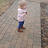 blonde_hair, boots, brick_path, candid, car_wheel, child, cool_weather, curious_expression, girl, grass, outdoors, pavement, pink_jacket, profile_view, sidewalk, small_shoes, standing, stick, toddler, young_child