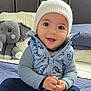 Emiliano is registered to the contest to win money with this photo: baby, child, smiling, hat, vest, blue_clothing, knit_hat, dinosaur_print, bed, blanket, toy_elephant, stuffed_animal, indoor, happy, cute, portrait, sitting, infant, warm_clothing, face