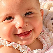 Lily is registered to the contest to win money with this photo: baby, child, infant, smiling, happy, portrait, close_up, face, eyes, floral_clothing, pink, teddy_bear, stuffed_animal, blanket, soft_lighting, indoor, warm_tones, lying_down, adorable, photography