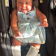 Emily is registered to the contest to win money with this photo: baby, infant, child, portrait, car_seat, sitting, dress, blue_dress, white_bows, hair_bows, socks, smiling, facial_expression, indoor, sunlight, vehicle, safety_seat, fashion, wood_floor, photograph