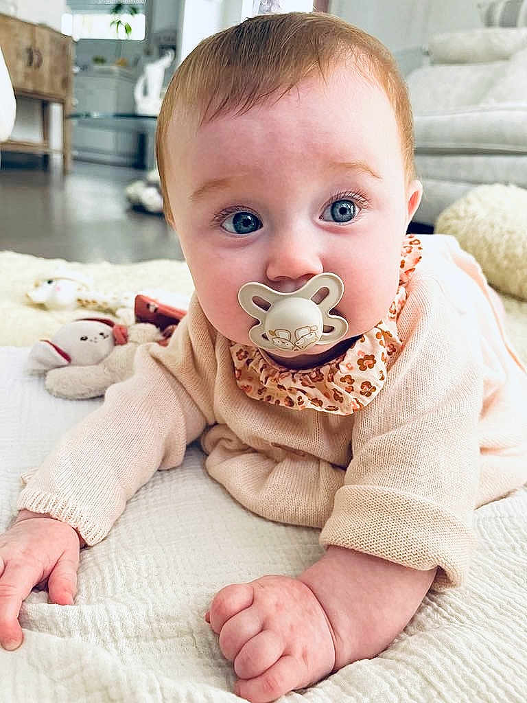 Hilda participe au concours pour gagner de l'argent avec cette photo : baby, pacifier, crawling, blanket, plush_toy, indoor, living_room, child, curious, soft_lighting, cozy, furniture, carpet, clothing, person, face, hand, blue_eyes, cute, infant