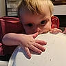 toddler, child, face, hand, high_chair, plate, indoor, curious, baby, portrait, furniture, wall_art, room, person, skin, table, light, hair, expression, home
