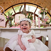 Talya participe au concours pour gagner de l'argent avec cette photo : baby, smiling, white_dress, flower_headband, candle, cake, cross, flowers, celebration, table, decorations, happy, indoors, portrait, child, event, cute, joyful, party, ceremony