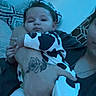 Everleigh is registered to the contest to win money with this photo: baby, infant, cow_print, onesie, tattoo, hand, adult, holding, pillow, couch, indoor, person, child, portrait, relaxing, pattern, blue_tint, comfort, casual, home