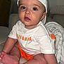 baby, child, infant, cap, white_tshirt, orange_shorts, sitting, couch, blanket, indoors, cute, face, hand, foot, curious, wide_eyes, soft_lighting, skin, clothing, portrait
