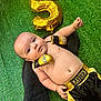 baby, infant, boxing_gloves, boxing_shorts, gold_balloon, number_5_balloon, green_turf, towel, cute, child, celebration, portrait, outdoor, sportswear, playful, happy, small_child, person, lying_down, costume