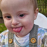 Caleb joined the competition — help win amazing prizes! baby, buttons, child, clothing, cute, daylight, dinosaur_patch, expression, face, fence, garden, greenery, outdoor, overalls, person, playful, seat, smiling, toddler, tongue
