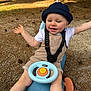 toddler, child, toy_car, hat, bucket_hat, overalls, outdoor, playground, happy, smiling, arms_outstretched, sunlight, nature, ground, play, fun, person, baby_shoes, casual_clothing, daytime