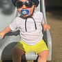 toddler, child, sunglasses, hat, pacifier, slide, playground, white_shirt, yellow_shorts, sneakers, outdoor, sunlight, shadow, smiling, casual_clothing, summer, fun, play, cute, young_kid