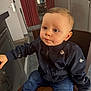 toddler, child, indoor, jacket, blue_jeans, chair, curious, sitting, brown_chair, casual_clothing, young_child, expression, face, short_hair, floor, door, curtains, home_interior, person, footwear