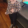 black_leggings, braided_hair, casual_clothing, child, cute, girl, gray_boots, happy, home, indoors, person, plaid_shirt, playful, portrait, smiling, standing, toddler, tv_stand, wooden_floor, young_child